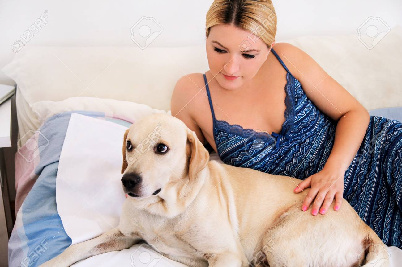Mujer Con Su Perro En La Cama En Casa, Relajándose En El Dormitorio. Joven  Mujer Hermosa Juega En La Cama Con Su Perro. El Labrador Retriever Amarillo  Se Metió En La Cama