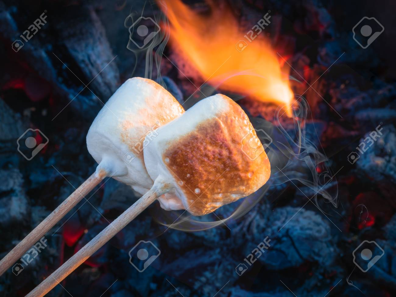 two brown sweet marshmallows roasting over fire flames marshmallow