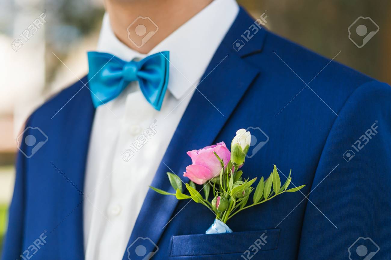 El novio elegante del primer arropado en chaqueta azul y la camisa blanca en el parque el día de su boda. Enfoque en rosa boutonniere El novio elegante del primer arropado en chaqueta azul y la camisa blanca en el parque el día de su boda. Enfoque en rosa boutonniere