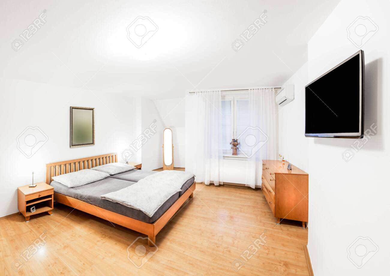 Ordinary Bedroom Of The House In Wooden Style With Double Bed, Bedside  Tables, Mirror, Chest Of Drawers And A Modern TV. Bedroom Is Lit By Bright  Light Mounted On The Ceiling And, image size:1300x920