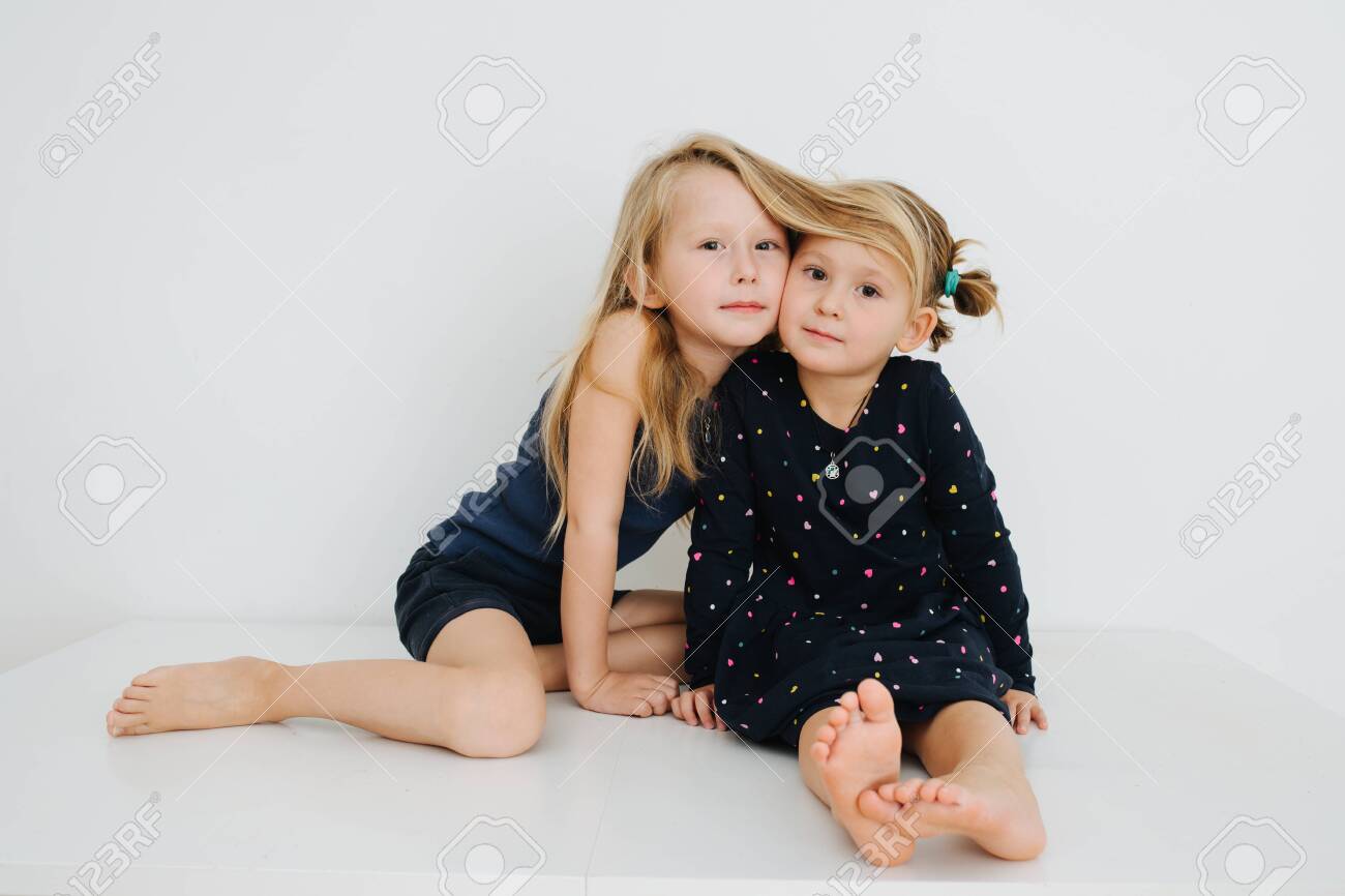 Lovely little barefoot siblings lying on a table with their feet up. Over white wall. Touching cheeks. Both in nightware. - 143650372 Lovely little barefoot siblings lying on a table with their feet up. Over white wall. Touching cheeks. Both in nightware. - 143650372