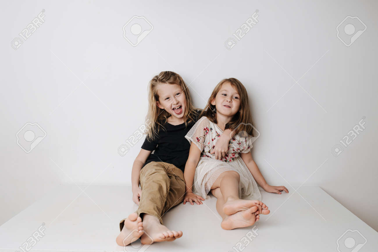 Naughty boy hugs girl, she leans away. Siblings sitting together on a table. - 159990096 Naughty boy hugs girl, she leans away. Siblings sitting together on a table. - 159990096